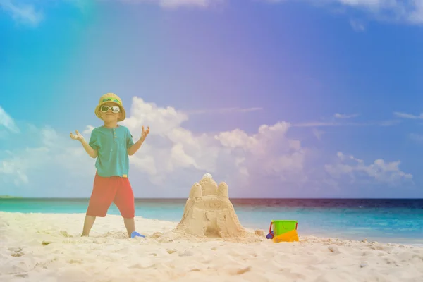 Szczęśliwy chłopczyk z zbudowany zamek z piasku na plaży — Zdjęcie stockowe