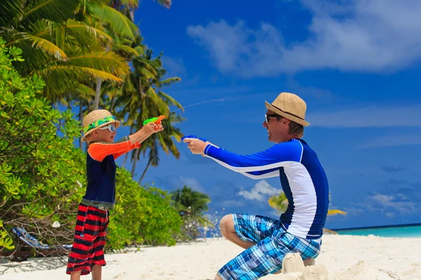 पिता और बेटा समुद्र तट पर पानी की बंदूक के साथ खेल रहे हैं — स्टॉक फ़ोटो, इमेज
