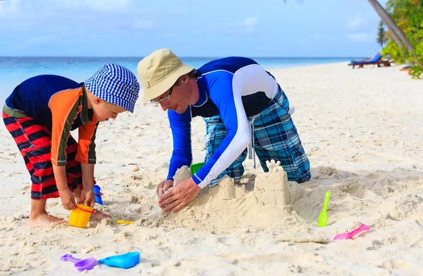 Vader en zoon gebouw zand kasteel op tropisch strand — Stockfoto