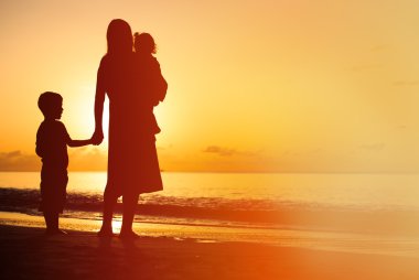 mother and two kids walking on beach at sunset clipart