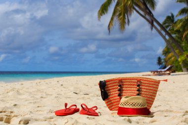şapka, güneş gözlüğü ve tropikal bir plajda flip flop