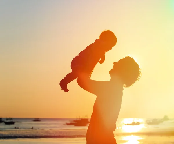 Vader en kleine dochter silhouetten op zonsondergang strand — Stockfoto