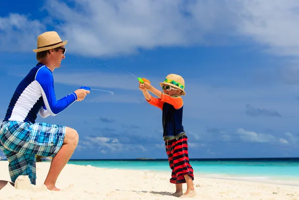 Vader en zoon spelen met water geweren op het strand — Stockfoto