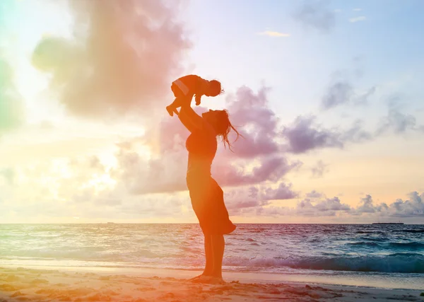 Šťastná matka a dítě baví na pláži při západu slunce — Stock fotografie