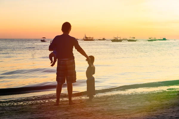 Pai e crianças silhuetas na praia ao pôr do sol — Fotografia de Stock