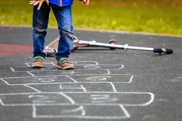 Gamin jouer marelle sur aire de jeux en plein air — Photo