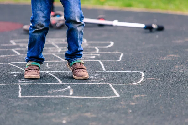 Gamin jouer marelle sur aire de jeux en plein air — Photo