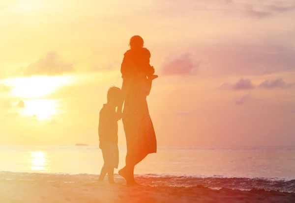 Мать и двое детей прогуливаются по пляжу на закате — стоковое фото
