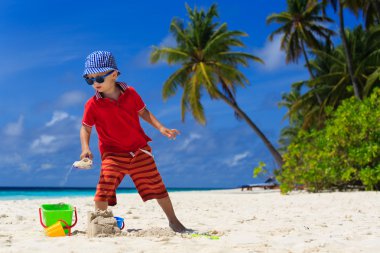 Küçük çocuk kumsalda kumla oynuyor.