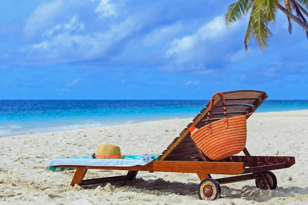Chapéu de palha e saco em uma cadeira lounge na praia tropical — Fotografia de Stock