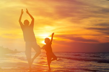 Baba ve oğul günbatımı denizde yoga yaparken