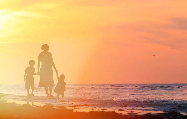Mère et deux enfants marchant sur la plage au coucher du soleil — Photo