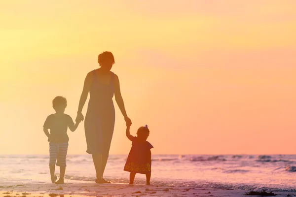 Moeder en twee kinderen wandelen op het strand bij zonsondergang — Stockfoto