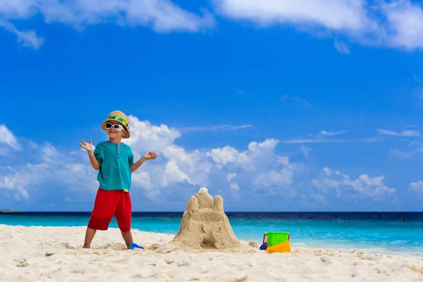 Criança feliz com castelo de areia construído na praia — Fotografia de Stock