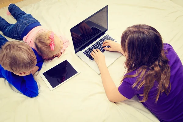 Mutter arbeitet am Laptop, während Kinder auf Touchpad schauen — Stockfoto