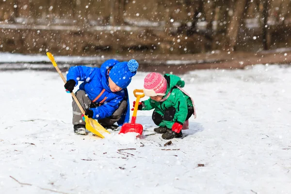 Malý chlapec a dívka kopání sněhu v zimě — Stock fotografie