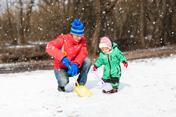 Father and little daughter digging snow in winter park — Stock Photo, Image