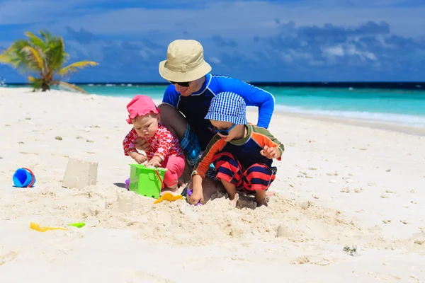 Отец и дети строят замок из песка на тропическом пляже — стоковое фото
