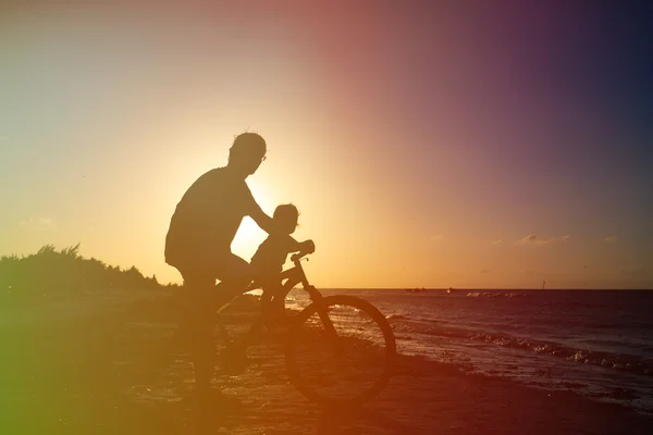 Père et bébé faire du vélo au coucher du soleil mer — Photo