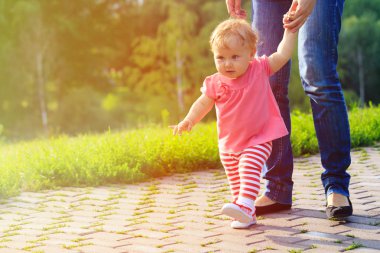 first steps of little girl with mother outdoors clipart