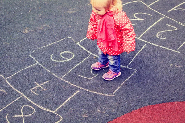 สาวน้อยเล่นฮ็อปสก็อตช์บนสนามเด็กเล่นข้างนอก — ภาพถ่ายสต็อก
