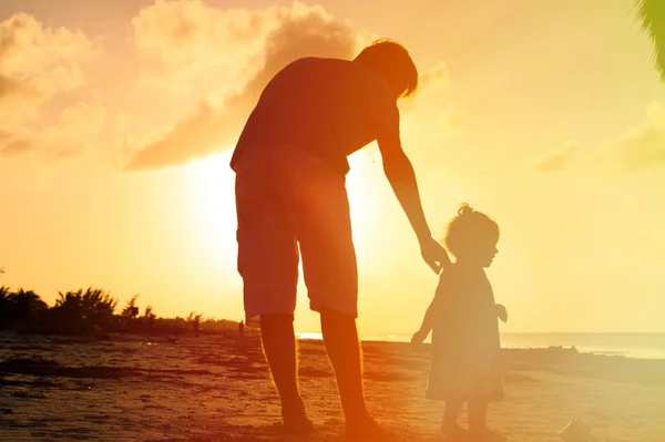 Vater und kleine Tochter spazieren bei Sonnenuntergang am Strand — Stockfoto