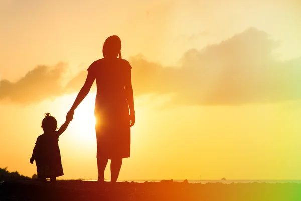 Mor och liten dotter går på stranden vid solnedgången — Stockfoto