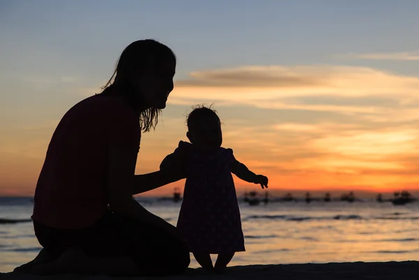 Silhouette di madre e figlia sulla spiaggia al tramonto — Foto Stock