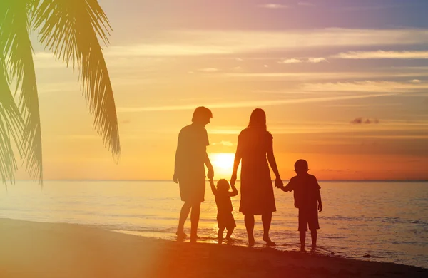 Счастливая семья с двумя детьми, гуляющими на закатном пляже — стоковое фото