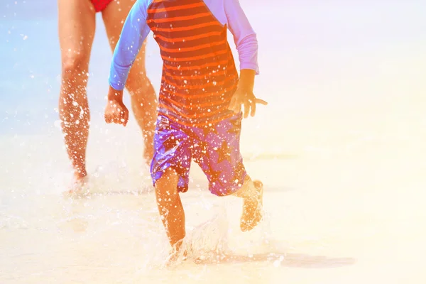 Niño pequeño con la madre jugando salpicaduras de agua en la playa — Foto de Stock