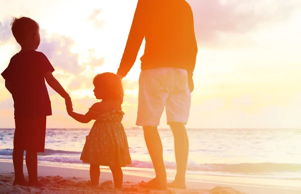 Vader en twee kinderen lopen op het strand bij zonsondergang — Stockfoto