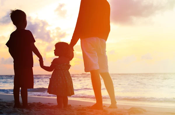 Baba ve iki çocuk gün batımında sahilde yürüyüş — Stok fotoğraf