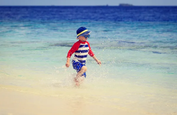 Piccolo ragazzo spruzzi d'acqua sulla spiaggia tropicale — Foto Stock