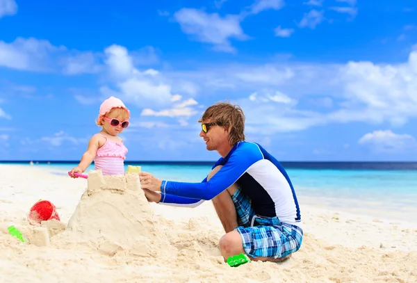 Vader en kleine dochter gebouw sandcastle op strand — Stockfoto