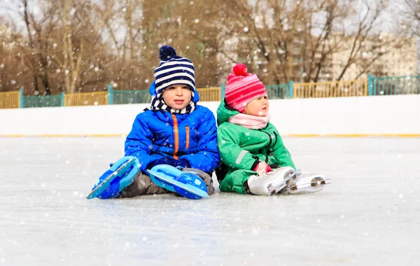 Μικρό αγόρι και κορίτσι που κάθεται στον πάγο με πατίνια — Φωτογραφία Αρχείου