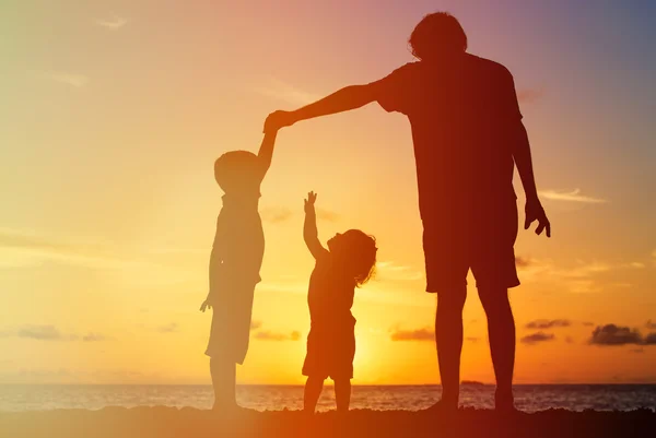 Pai e duas crianças brincando na praia do pôr do sol — Fotografia de Stock