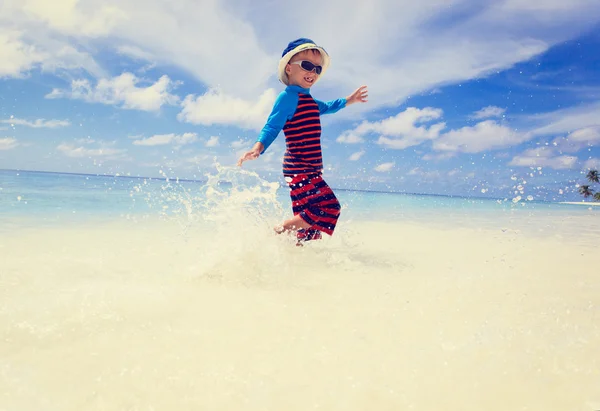 Pieni poika roiskuu vettä trooppisella rannalla — kuvapankkivalokuva