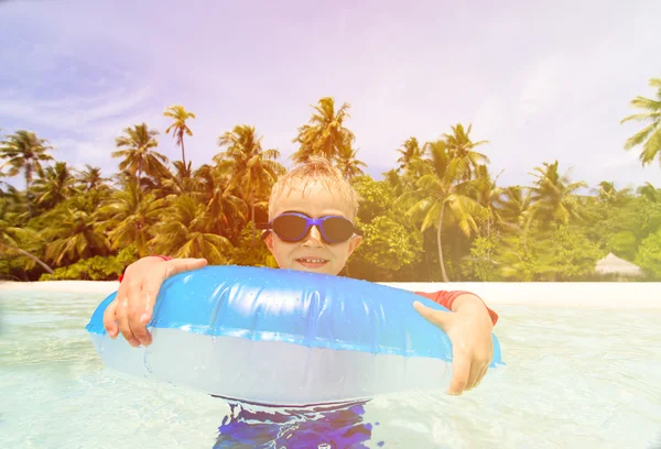 Счастливый мальчик с жизнерадостным кольцом веселится на пляже — стоковое фото