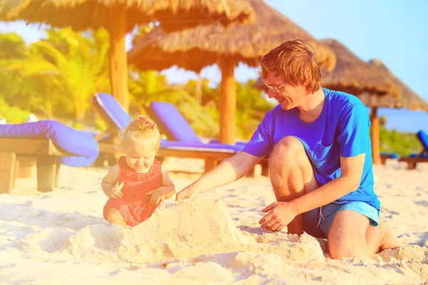 Isä ja pieni tytär rakennus hiekkalinna rannalla — kuvapankkivalokuva