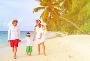 tropikal kumsalda yürüyen iki çocuklu aile