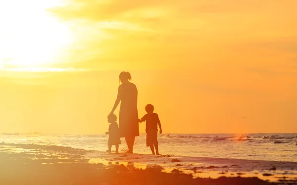 Madre y dos niños caminando en la playa al atardecer — Foto de Stock
