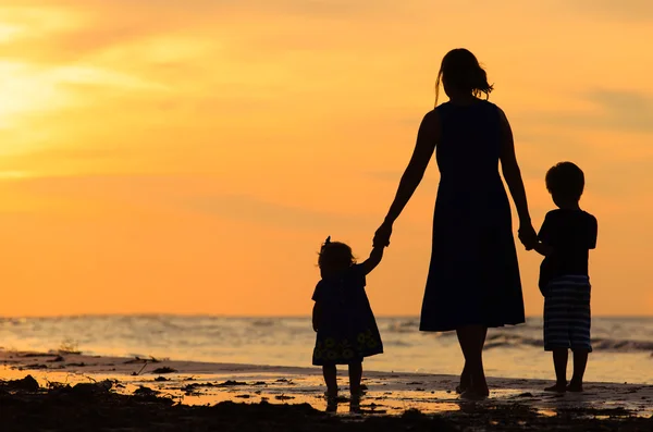 Mère et deux enfants marchant sur la plage au coucher du soleil — Photo