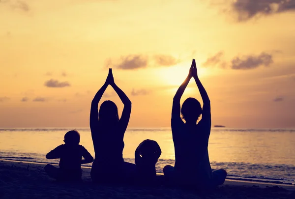 Silhouettes familiales faisant du yoga au coucher du soleil — Photo