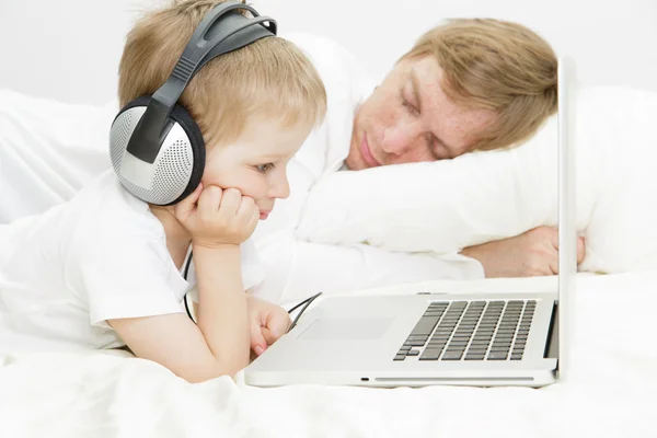 Barn i hörlurarna med datorn medan far sover — Stockfoto