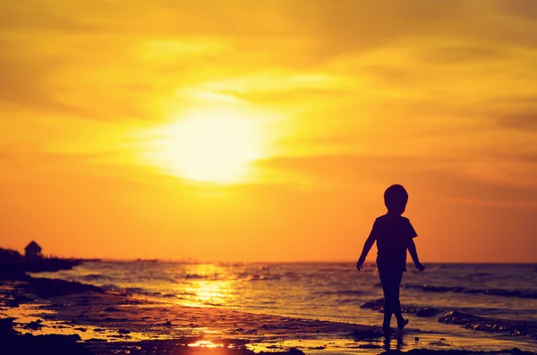 Liten pojke går på sunset beach — Stockfoto