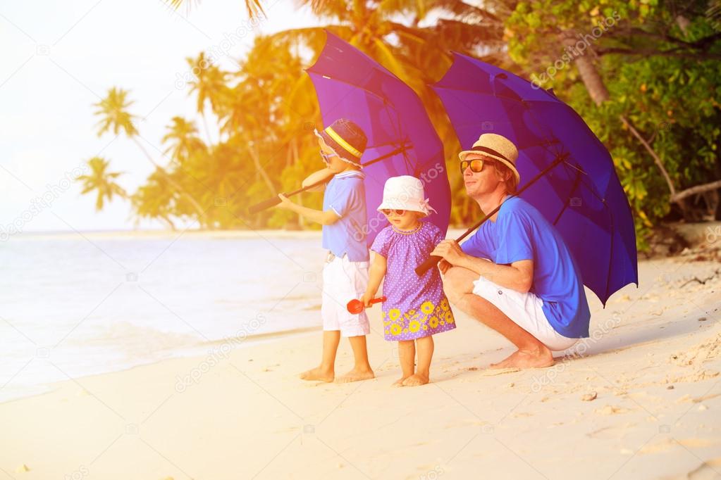 Father and two kids at beach with umbrellas