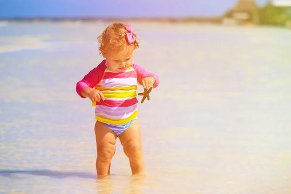 Niña sosteniendo estrellas de mar en la playa de verano — Foto de Stock
