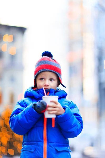 Маленький хлопчик має гарячий напій в зимовому місті Різдва — стокове фото
