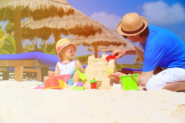 Vader en kleine dochter gebouw sandcastle op strand — Stockfoto