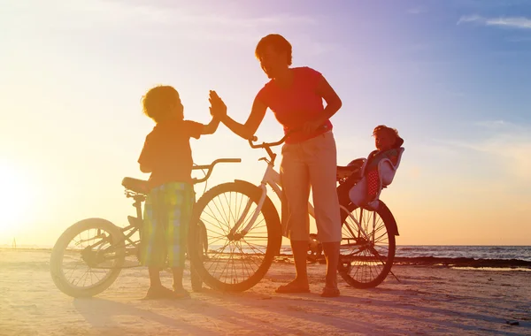 Mãe feliz com crianças de bicicleta ao pôr do sol — Fotografia de Stock